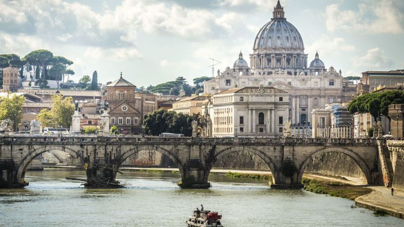 Rom-Szene mit Petersdom, Brücke über den Tiber, Boot auf dem Fluss und historische Uferbebauung.