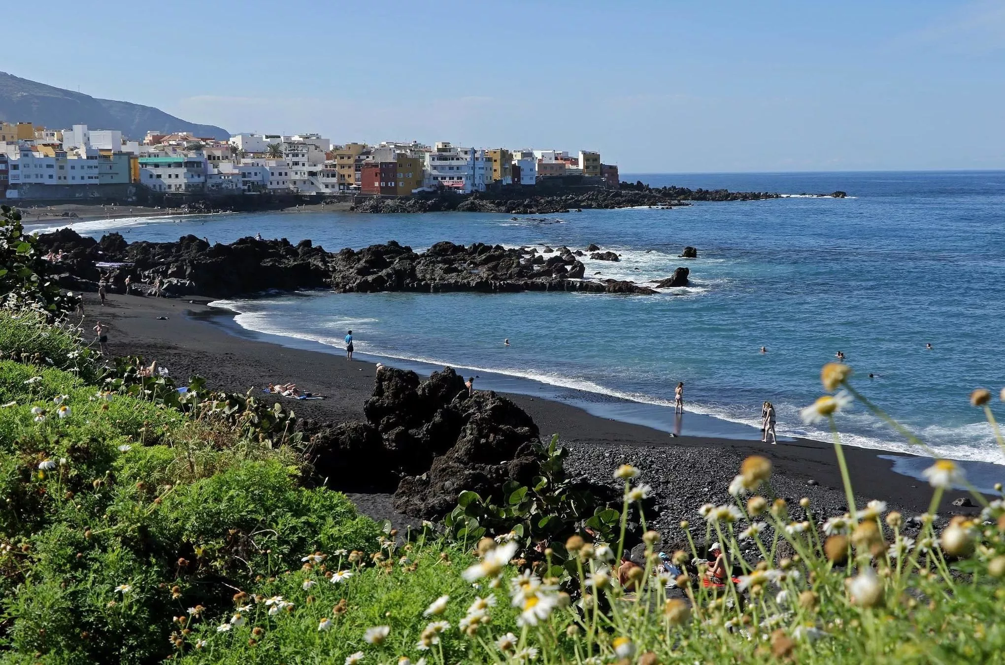Dunkler Vulkansand, kleine Felsen und tropische Pflanzen: Der Playa Jardín in Puerto de la Cruz zählt zu den schönsten Stränden auf Teneriffa