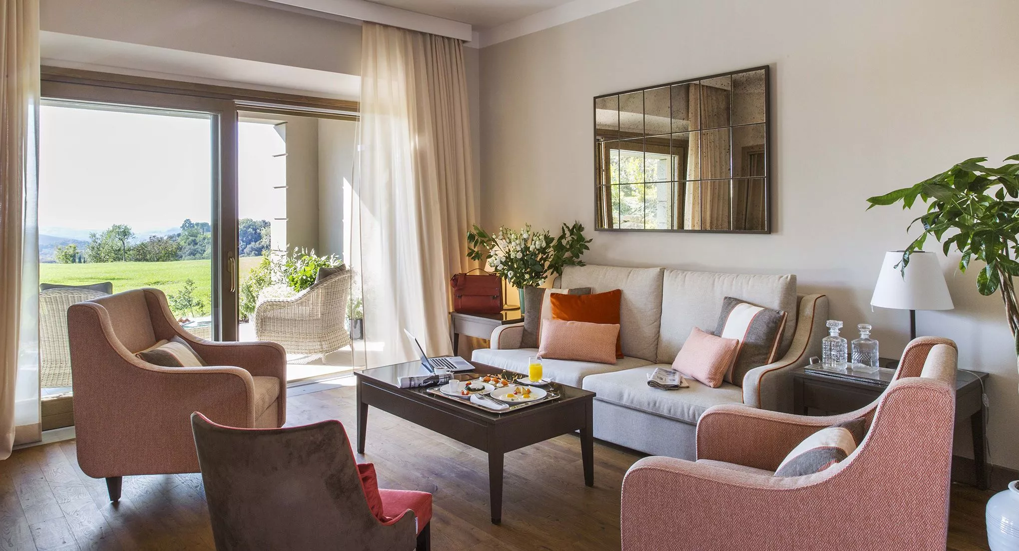 Blick in ein Zimmer des Resorts: warme Farben im Inneren, sattgrüne Toskana-Landschaft vor dem Fenster