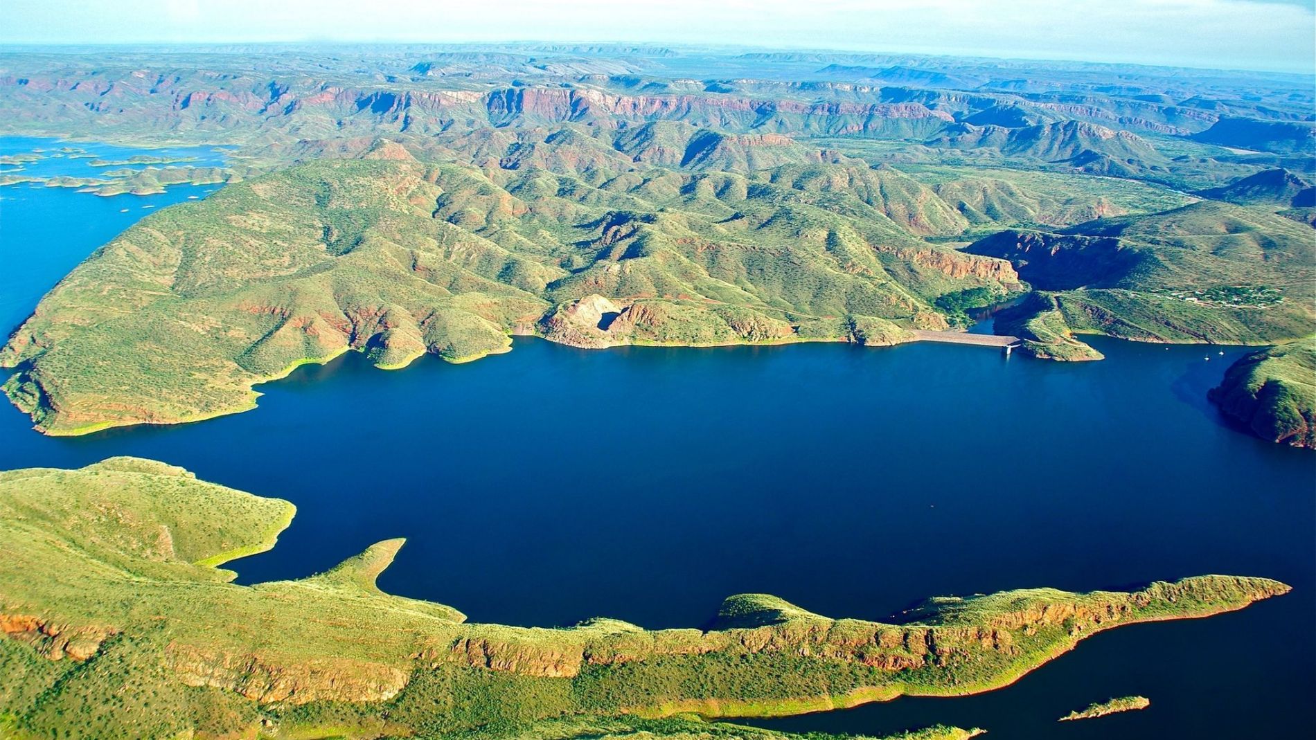Luftaufnahme einer Küstenlandschaft mit grünen Hügeln und Schluchten um einen großen blauen See.