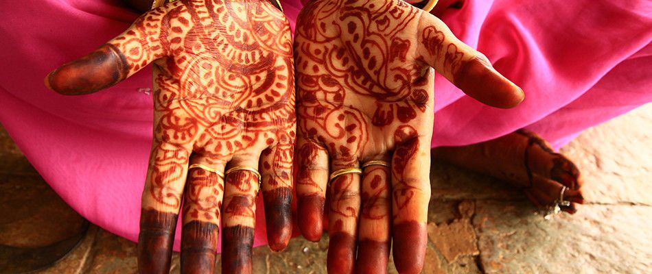 Nahaufnahme von Händen mit aufwendigem Henna-Design (Mehndi) und pinkem Stoff im Hintergrund.