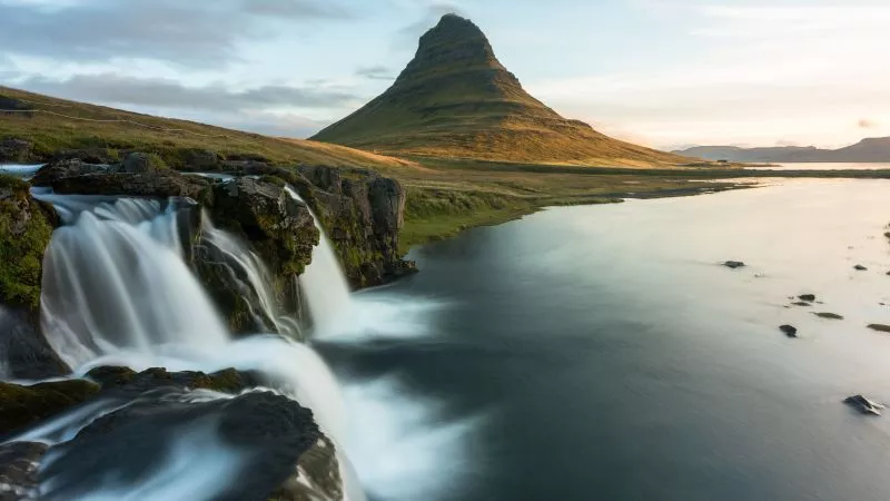 Isländische Landschaft: Wasserfall über Felsen in ruhigem Fluss, pyramidenförmiger Berg, Sonnenuntergang.