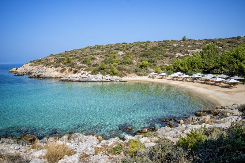Blaue Bucht von Six Senses Kaplankaya: Sandstrand, türkisfarbenes Wasser, Felsen, Sonnenliegen mit Schirmen.