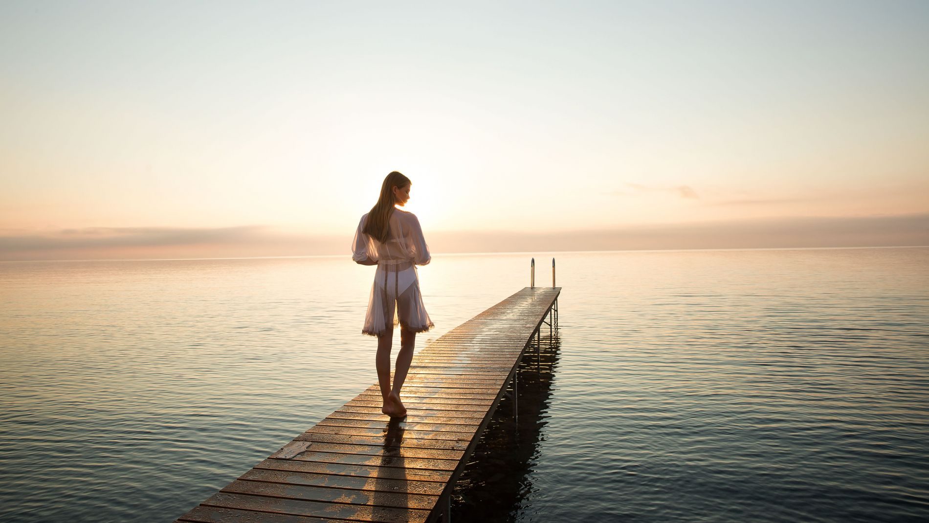 Frau barfuß auf einem Holzsteg am Domes Miramare Pier 2, Meer bei Sonnenuntergang, Blick zum Horizont.