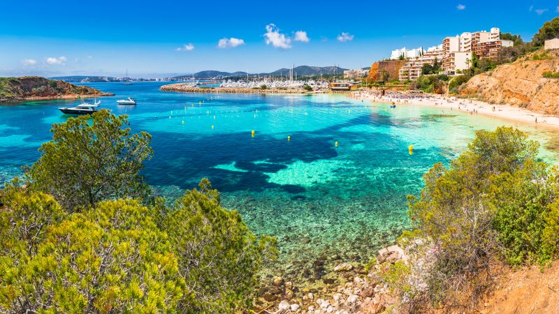 Puerto Portals Nous Strandpanorama mit türkisblauem Wasser, Yachten, Strand, Häusern am Hang und Bäumen. Puerto Portals Nous Strandpanorama mit türkisblauem Wasser, Yachten, Strand, Häusern am Hang und Bäumen.