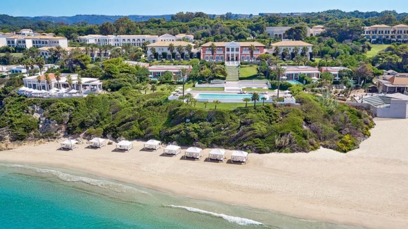 Luftaufnahme des Resorts Grecotel Mandola Rosa am Sandstrand mit Pool, Gartenanlagen und Strandliegen.