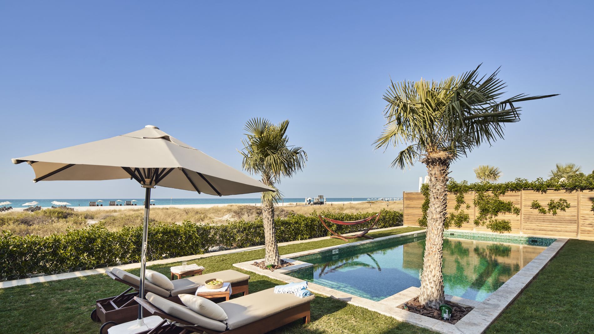 Privater Poolbereich mit Liegen, Sonnenschirm, Palmen; Blick auf Strand und Meer in den Vereinigten Arabischen Emiraten