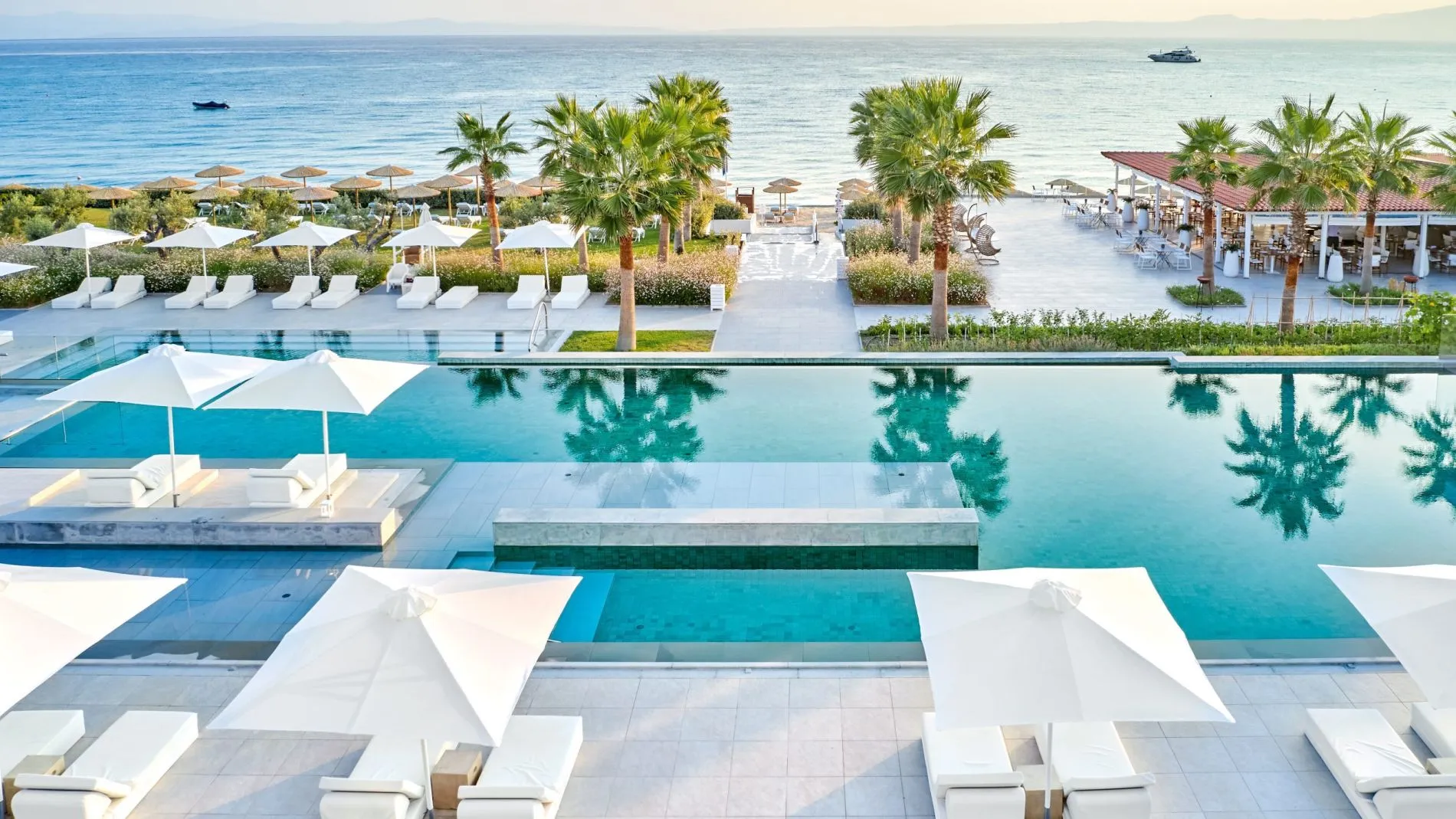 Infinity-Pool mit weißen Lounges, Sonnenschirmen und Palmen, Blick auf das Meer; Resort Domes Noruz Kassandra.