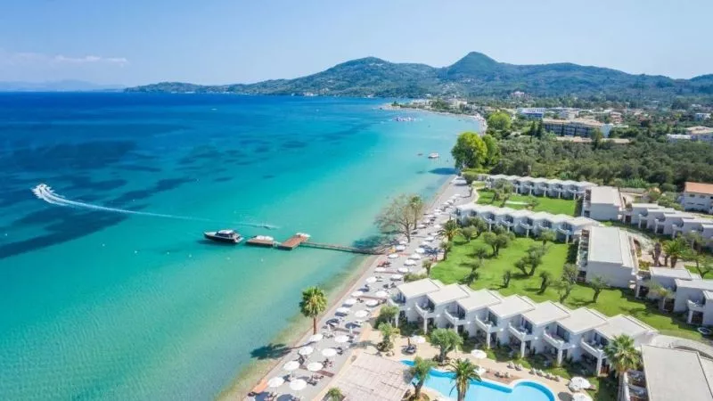 Luftaufnahme des Domes Miramare Resorts auf Korfu: Wasser, Strand mit Liegen, Pool und grüne Gartenanlagen.