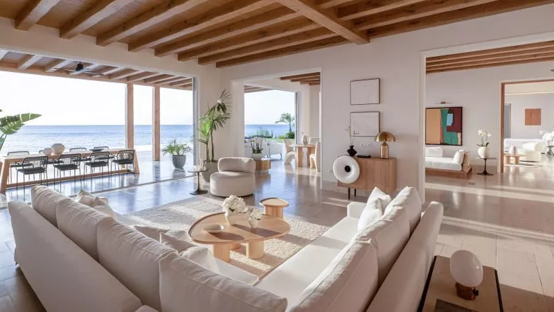 Großzügiger Wohnzimmerbereich mit weißen Sofas, Holzbalkendecke und Meerblick durch offene Terrasse, moderne Einrichtung.