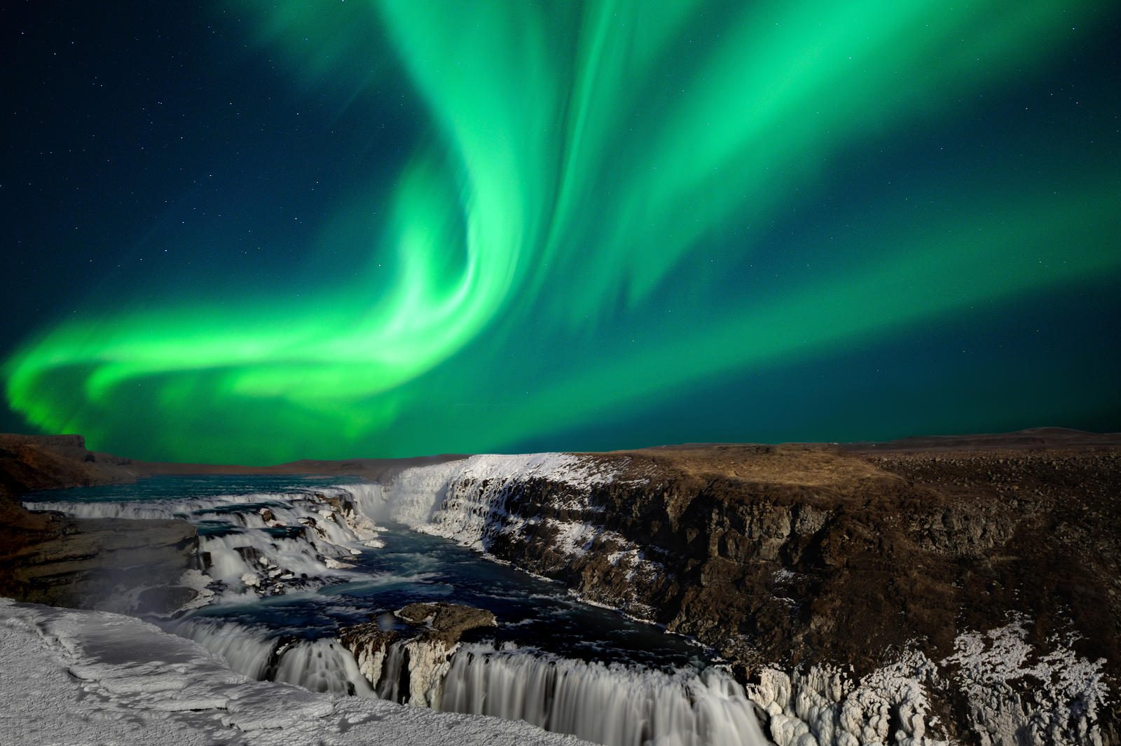 Nordlichter in grün über Gullfoss-Wasserfall, eisiger Canyon und tiefblaues Eis bei Nacht.
