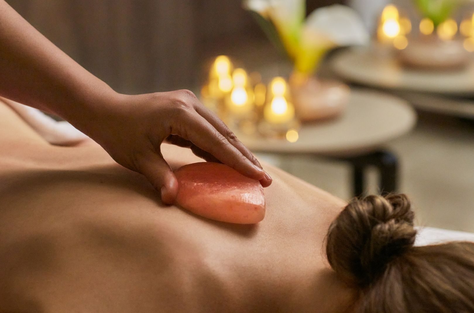 Rückenmassage mit warmem Stein im Explora Journeys Spa; Kerzenlicht schafft ruhige Atmosphäre.