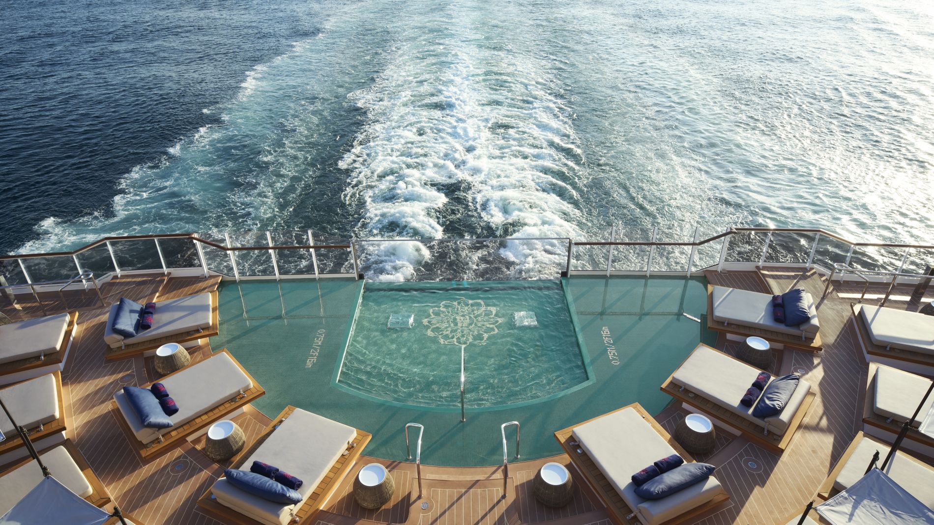 Heckdeck eines Explora Journeys-Schiffs; Pool umgeben von Sonnenliegen, Blick aufs offene Meer dahinter.