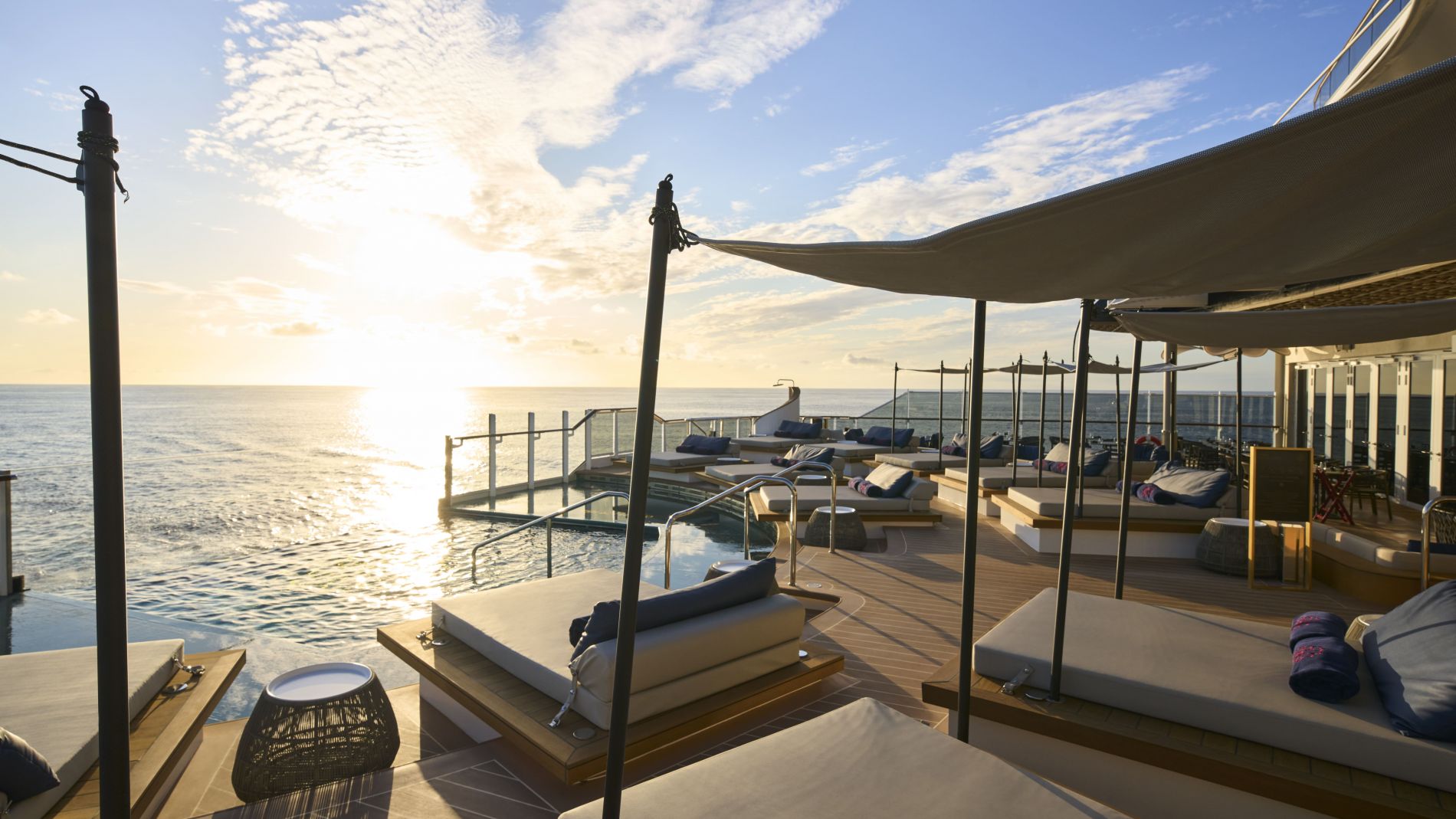 EXPLORA I Astern Pool Deck bei Sonnenuntergang; Liegen unter Sonnensegel, Infinity-Pool, Blick aufs offene Meer.
