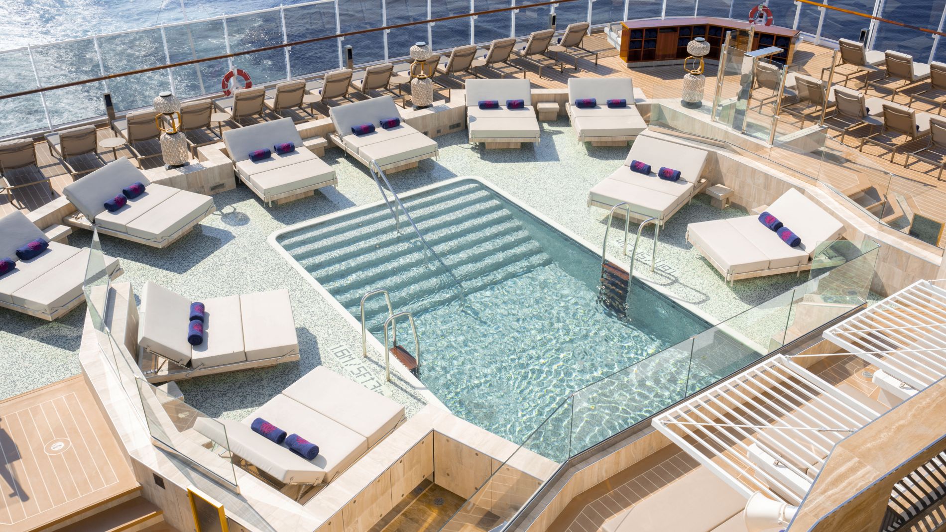 Außenpooldeck von Explora Journeys Kreuzfahrtschiff; Liegen ringsum, Glasgeländer, offenes Meer.
