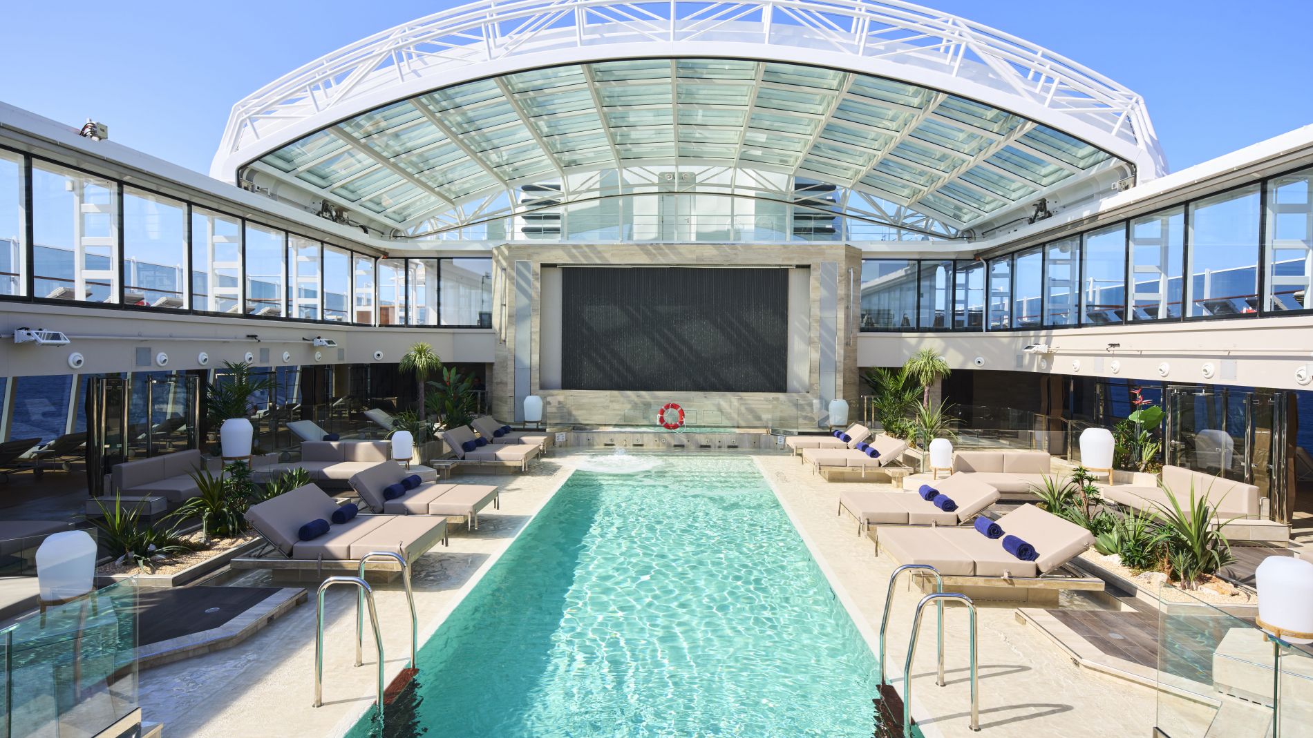 Poolbereich im Conservatory von Explora Journeys, Glasdach, Liegen und Lounge-Sitze.