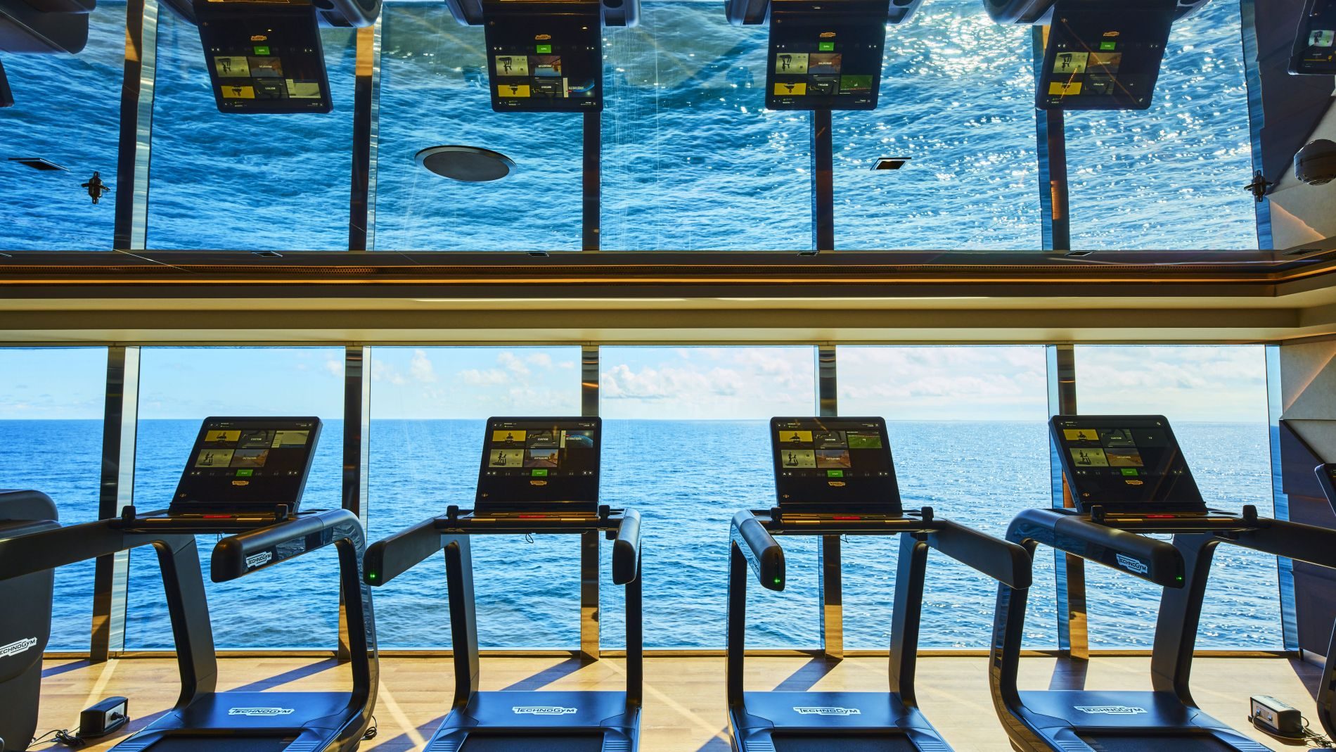 Vier Treadmills im Fitnessraum eines Explora Journeys Schiffes, Meerblick durch große Fenster.