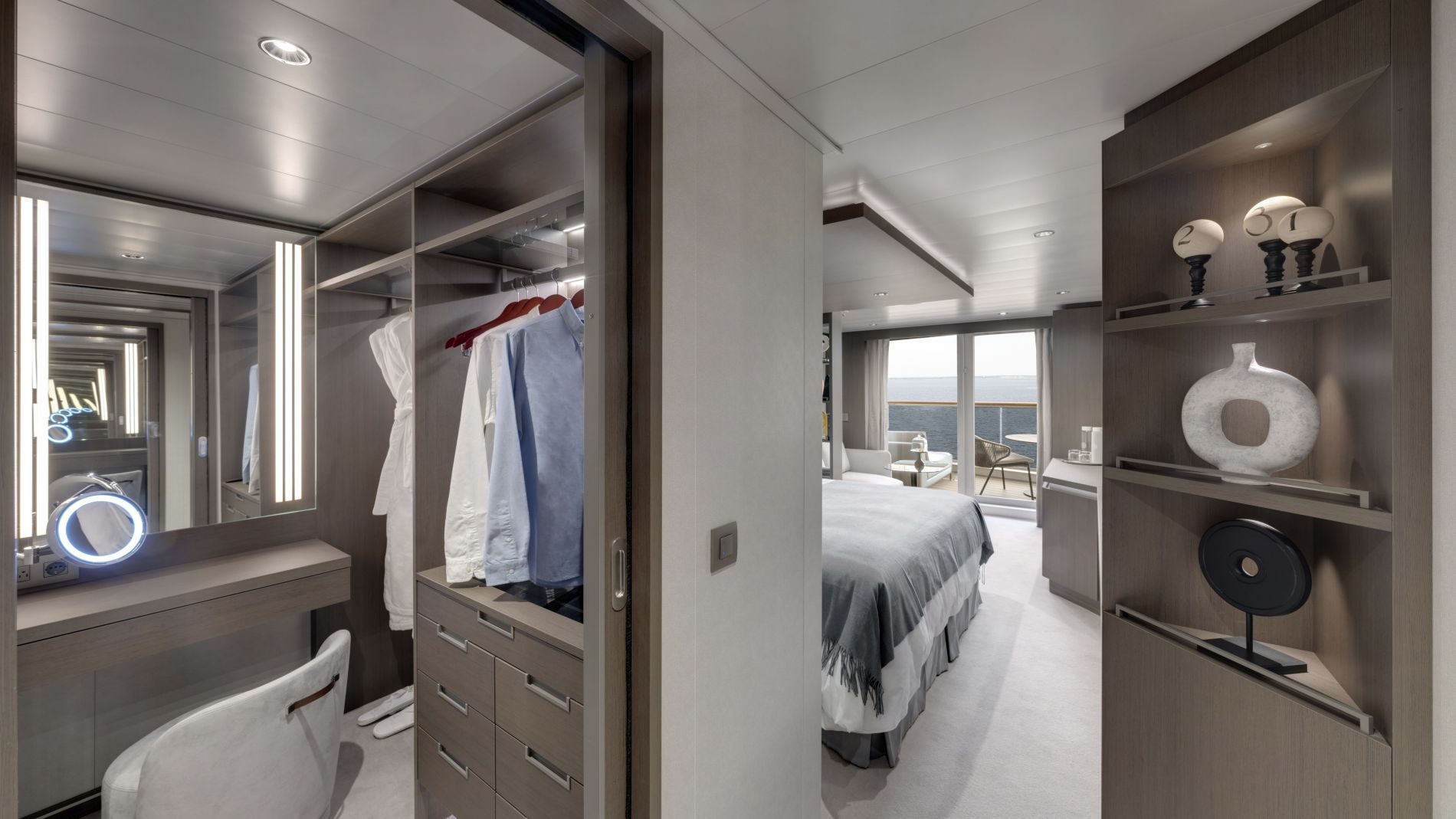 Explora Journeys Kabine mit Ankleidebereich, Kleiderschrank, Schminktisch mit Ringlicht, Bett und Meerblick-Balkon.