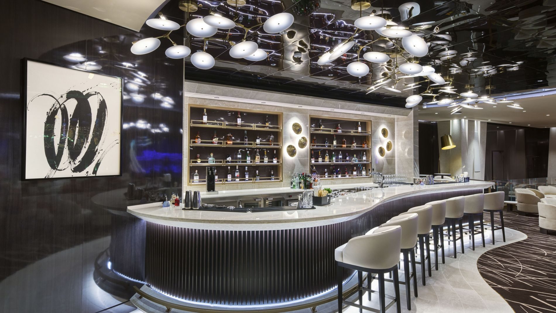 Barbereich der Explora Journeys Lounge mit rundem Marmortresen, Regalen voller Spirituosen und weißen Barhockern.
