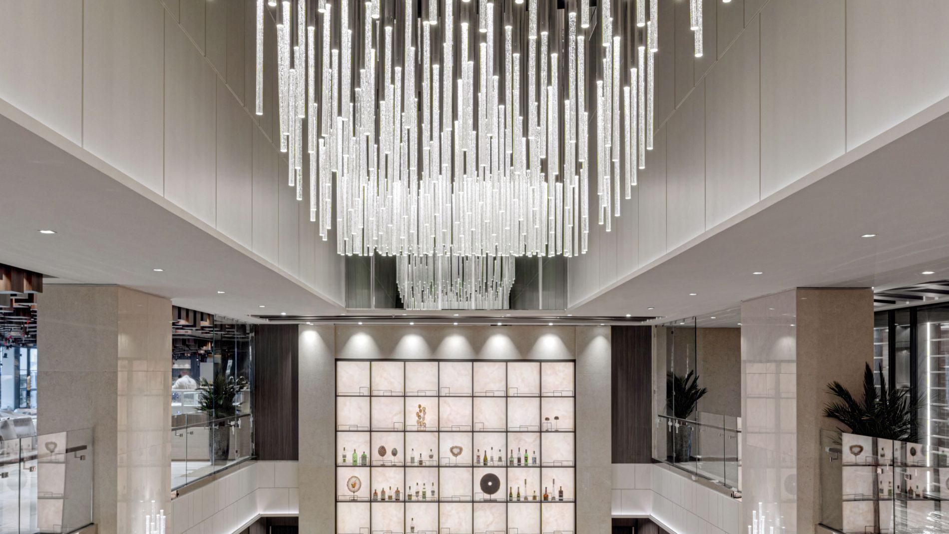 Großes Explora Journeys Lobby mit vielen vertikalen gläsernen Lichtstäben-Kronleuchter, Lounge-Bereich und Bar im Hintergrund