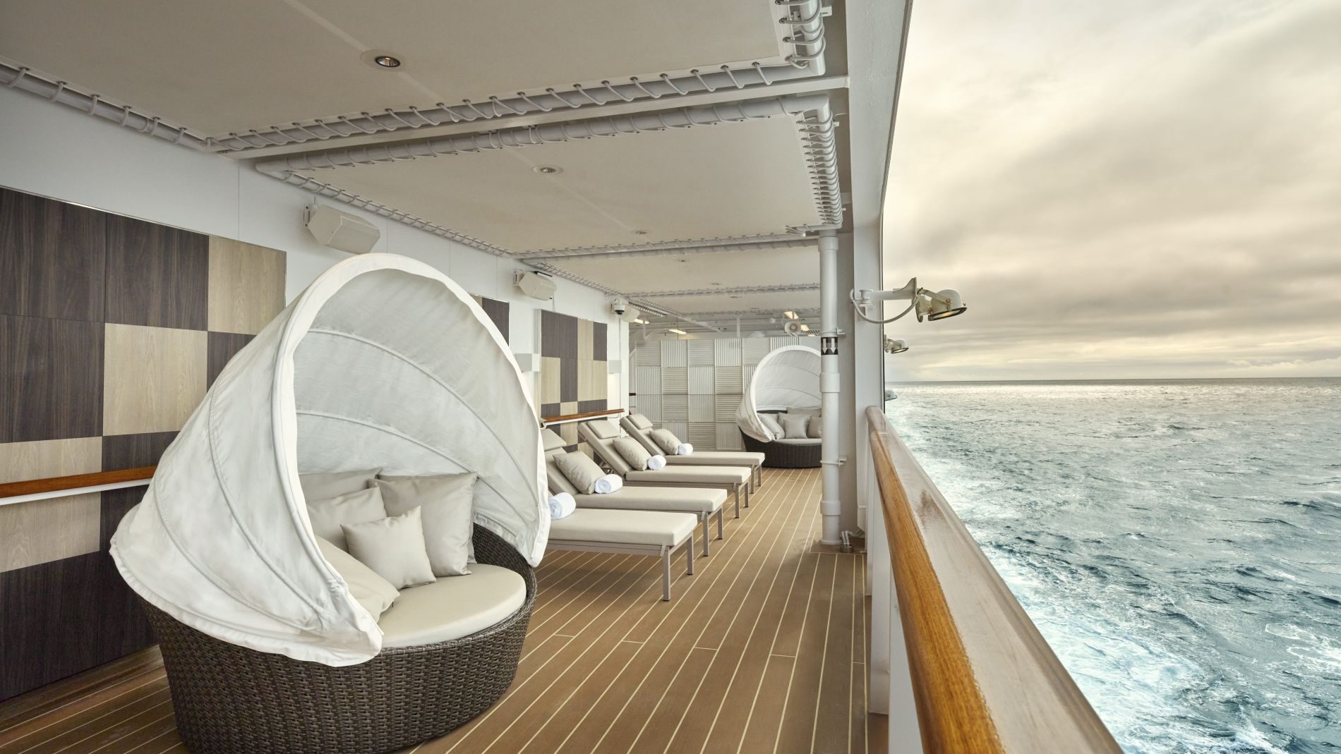 Decklounge an Bord eines Kreuzfahrtschiffs mit runden Korbsesseln, Liegen, Holzdeck und Meerblick. Decklounge an Bord eines Kreuzfahrtschiffs mit runden Korbsesseln, Liegen, Holzdeck und Meerblick.