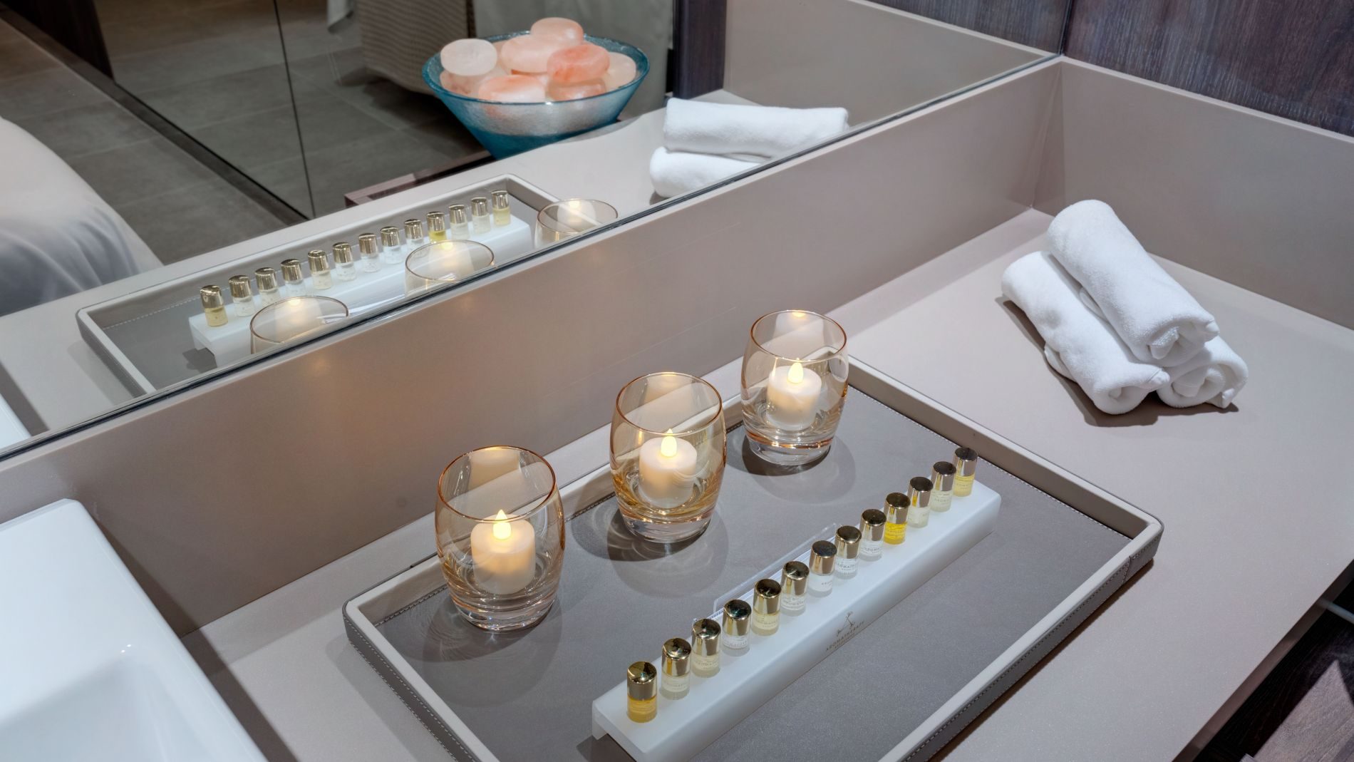 Badezimmerdetail mit Duftölen, drei Kerzen in Gläsern, weißen Handtüchern auf einer Ablage; Wellness-Atmosphäre (Explora Journeys)