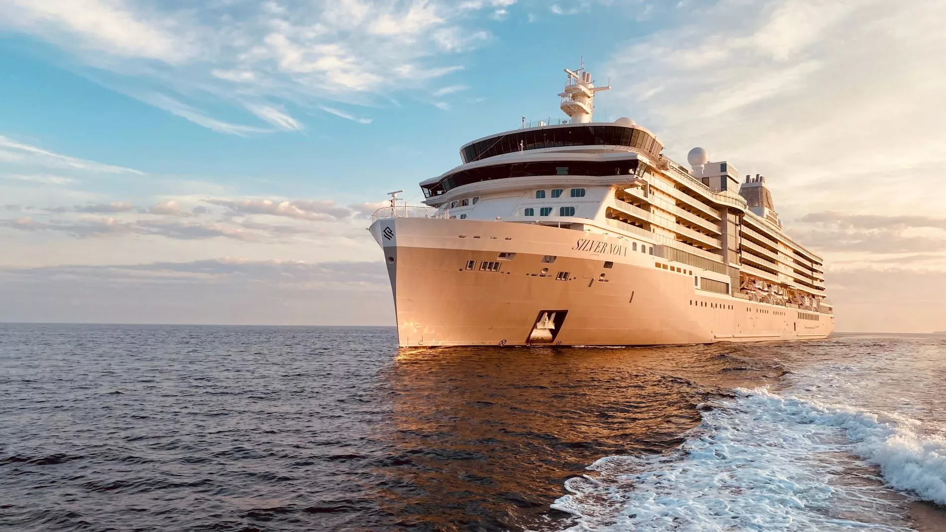 Großes weißes Kreuzfahrtschiff Silversea Nova fährt auf ruhiger See, Abendlicht reflektiert auf dem Rumpf.