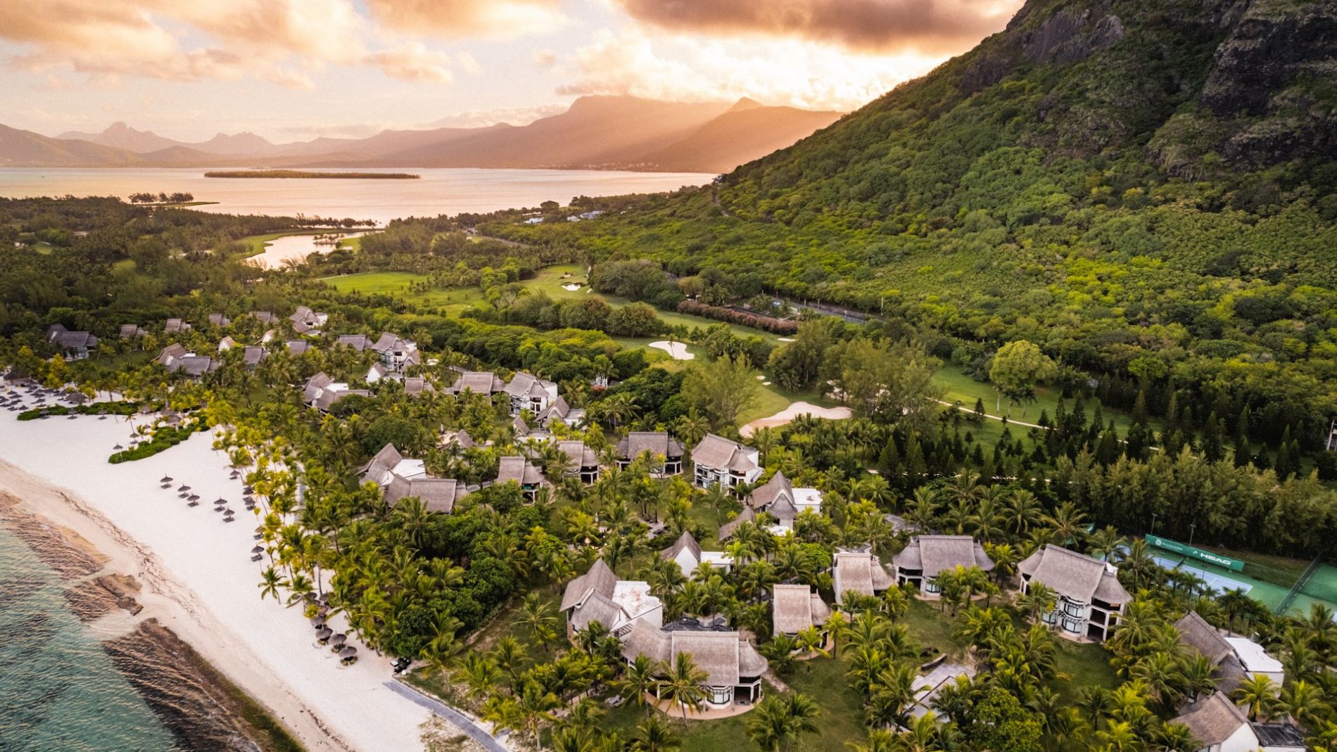 Luftaufnahme des Dinarobin Beachcomber Resorts am Strand mit Palmen, Bungalows und Berglandschaft bei Sonnenuntergang Luftaufnahme des Dinarobin Beachcomber Resorts am Strand mit Palmen, Bungalows und Berglandschaft bei Sonnenuntergang