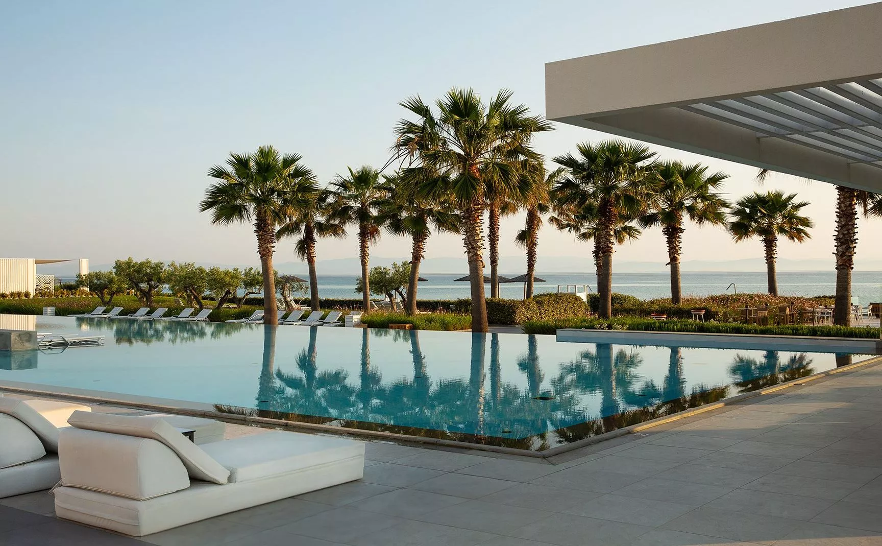 Poolanlage mit Palmen, Liegen am Rand und Meerblick; moderne Architektur am Domes Noruz Kassandra Pool.