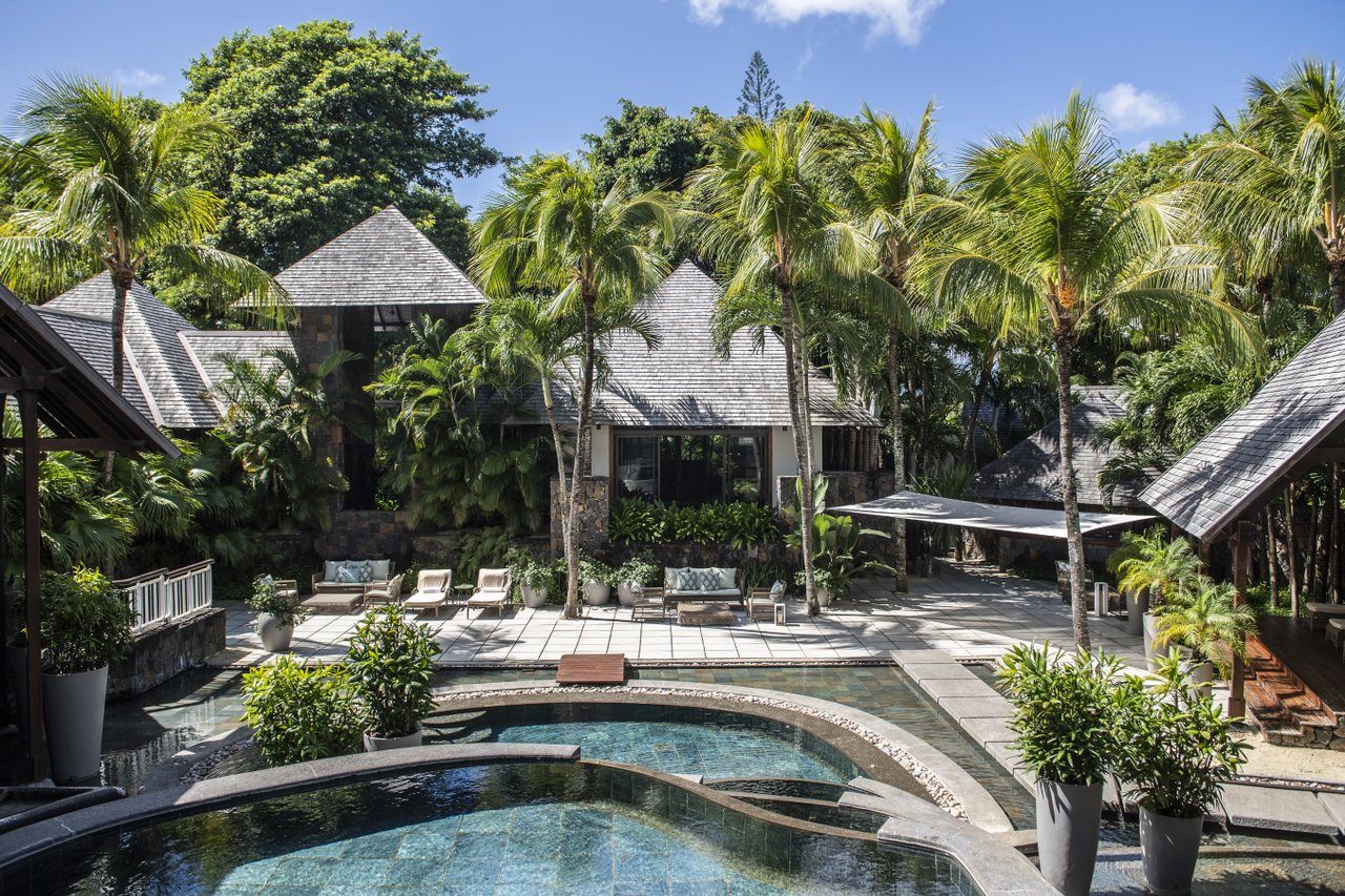 Spa-Außenbereich mit kurvigem Pool, Liegen, Palmen und strohgedeckten Bungalows umgeben von tropischem Garten Spa-Außenbereich mit kurvigem Pool, Liegen, Palmen und strohgedeckten Bungalows umgeben von tropischem Garten