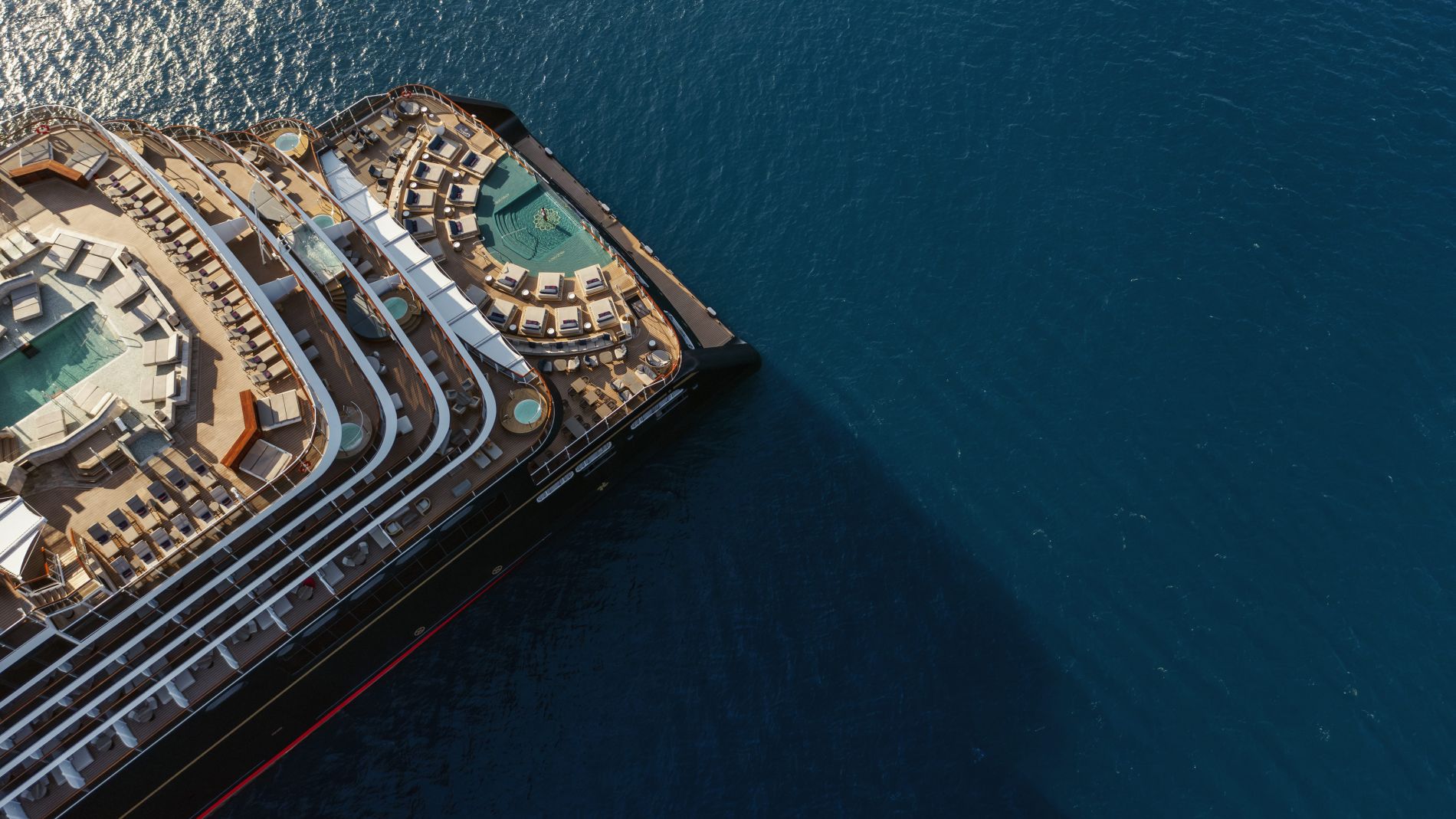 Luftaufnahme eines Kreuzfahrtschiffs von oben; Deck mit Sonnenliegen, Pools und Lounge-Bereichen am ruhigen blauen Meer. Luftaufnahme eines Kreuzfahrtschiffs von oben; Deck mit Sonnenliegen, Pools und Lounge-Bereichen am ruhigen blauen Meer.