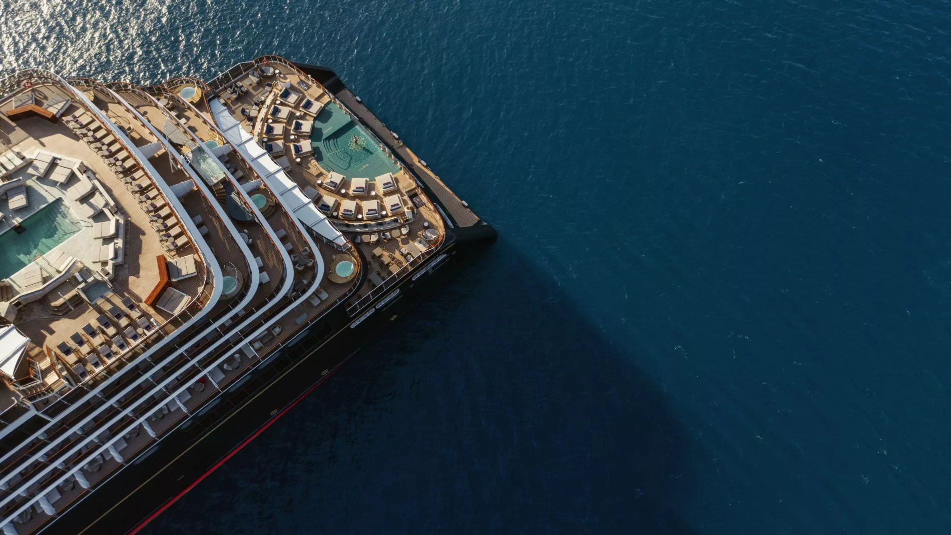 Luftaufnahme eines Kreuzfahrtschiffs von oben; Deck mit Sonnenliegen, Pools und Lounge-Bereichen am ruhigen blauen Meer. Luftaufnahme eines Kreuzfahrtschiffs von oben; Deck mit Sonnenliegen, Pools und Lounge-Bereichen am ruhigen blauen Meer.