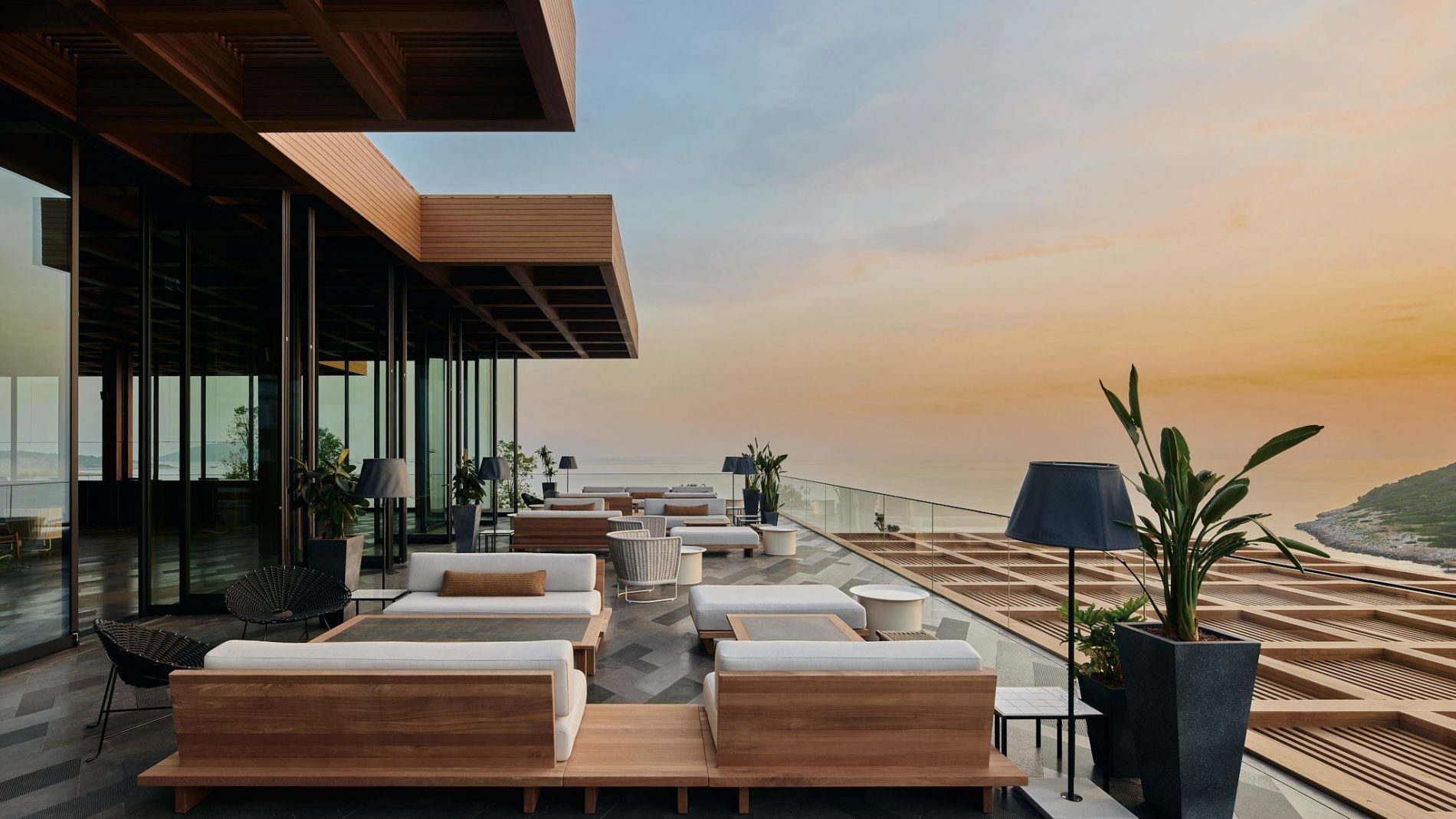 Terrassenlounge am Maxx Royal Bodrum: moderne Holzkonstruktion, Lounge-Möbel, Glasbrüstung, Meerblick bei Sonnenuntergang.