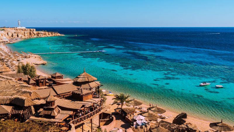Küstenabschnitt am Roten Meer in Sharm El Sheikh, Sinai: türkisfarbenes Wasser, Sandstrand mit Holzhütten und Booten am Ufer. Küstenabschnitt am Roten Meer in Sharm El Sheikh, Sinai: türkisfarbenes Wasser, Sandstrand mit Holzhütten und Booten am Ufer.