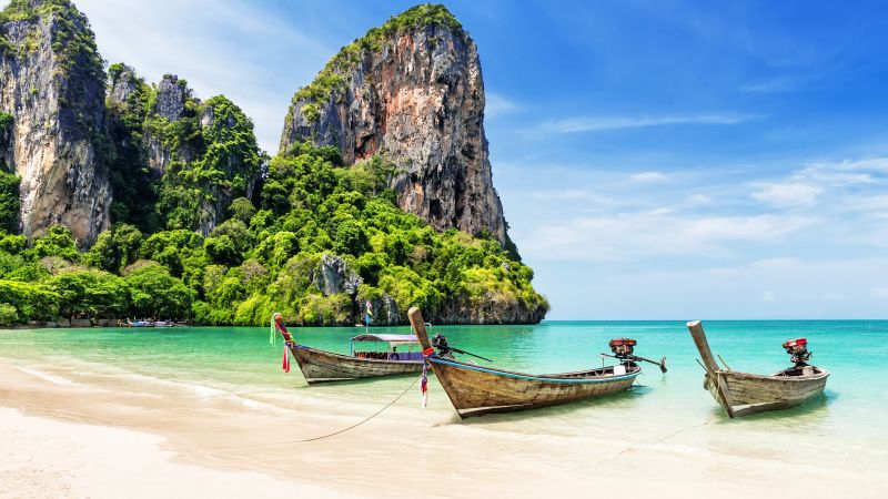 Thai Langtail-Boot im klaren türkisblauen Meer vor felsigen, grünen Klippen am Strand. Thai Langtail-Boot im klaren türkisblauen Meer vor felsigen, grünen Klippen am Strand.