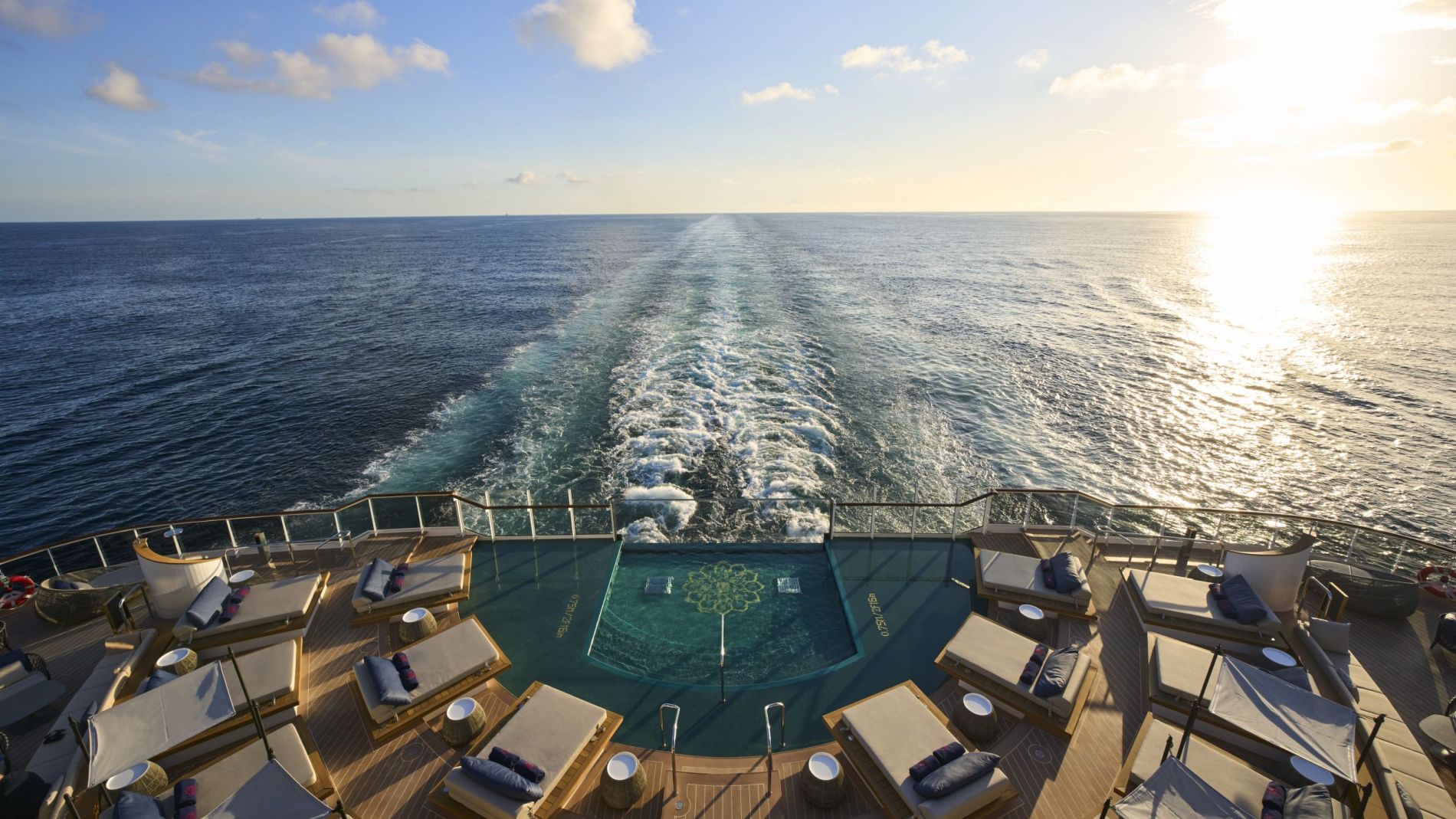 Achterdeck-Poolbereich eines Explora Journeys Schiffes mit Liegen, Sonnenliegen und Blick aufs Meer bei Sonnuntergang.