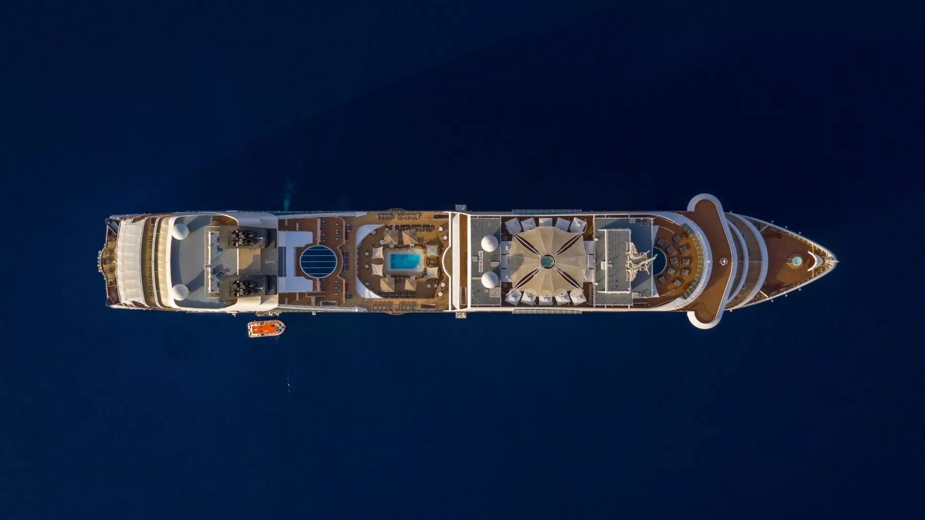 Luftaufnahme eines Seabourn-Kreuzfahrtschiffs von oben auf dunkelblauem Meer; Deck mit Pool, Liegen und Sonnensegeln.