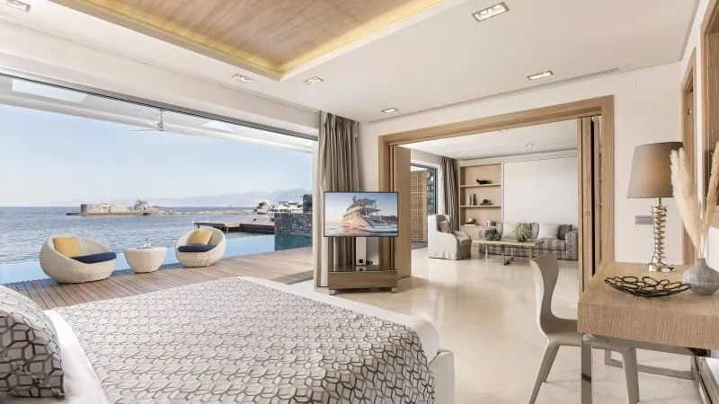 Schlafzimmer mit geometrischem Musterbett, offene Terrasse zum Meer, Pooldeck mit Lounge-Sesseln; Wohnzimmer mit TV und Regal.