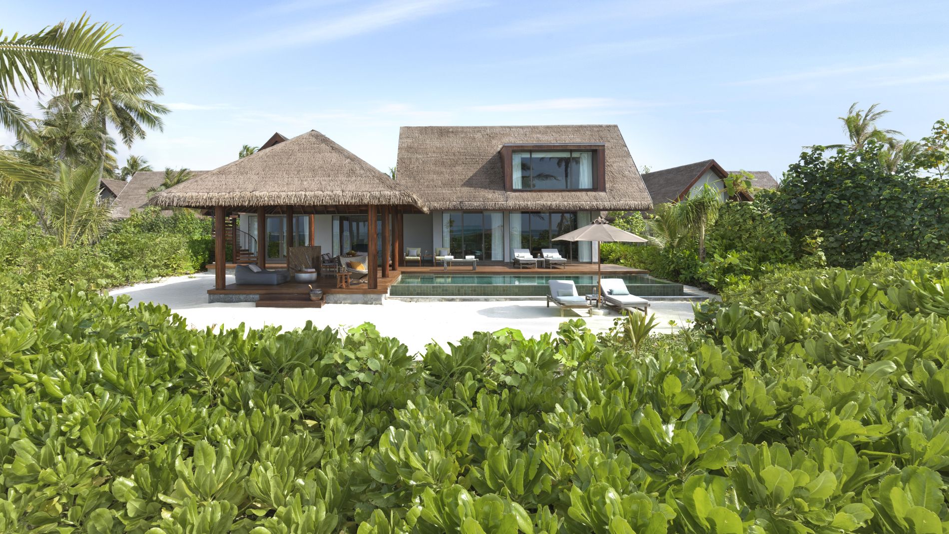 Villa mit Reetdach, Glasfronten und Terrasse, Poolbereich mit Liegen, Palmen am Strand; Teil eines Six Senses Resorts.