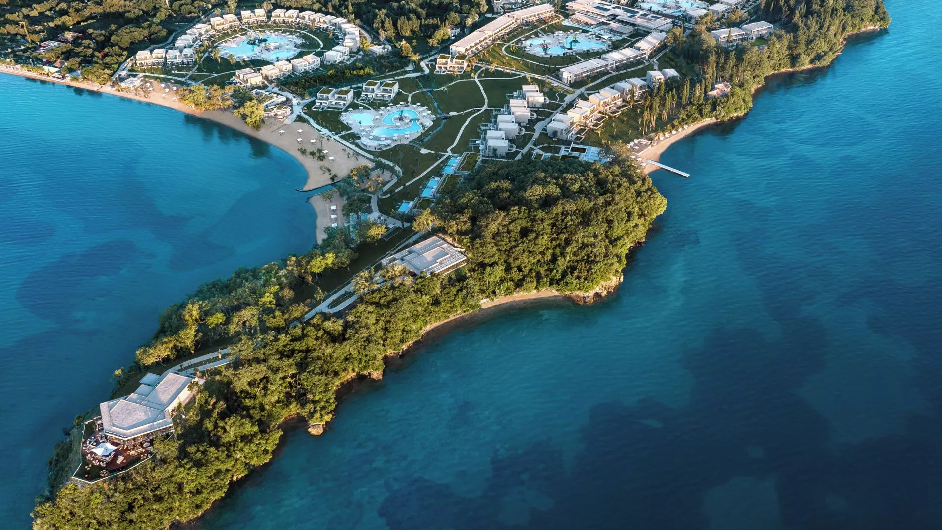 Luftaufnahme einer Resort-Halbinsel am Meer mit mehreren runden Pools, Bungalows, Strand und umgebendem Wald.