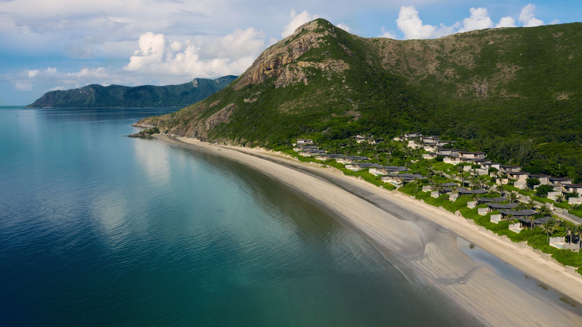 Luftaufnahme des Six Senses Resorts Con Dao: Strandbucht, Villen am Hang, türkisblaues Meer.