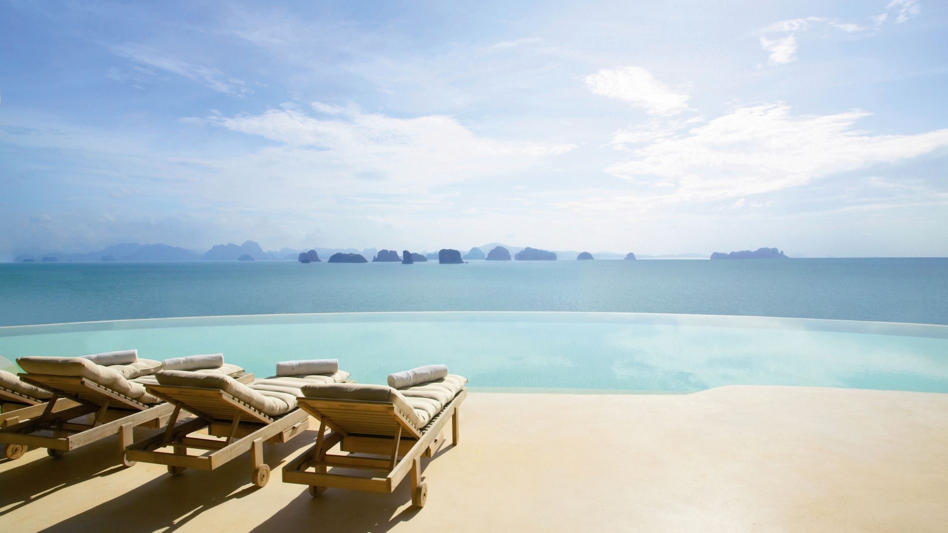 Infinity-Pool mit Meerblick und Inseln am Horizont; Beckenrand mit Liegen und Kissen.