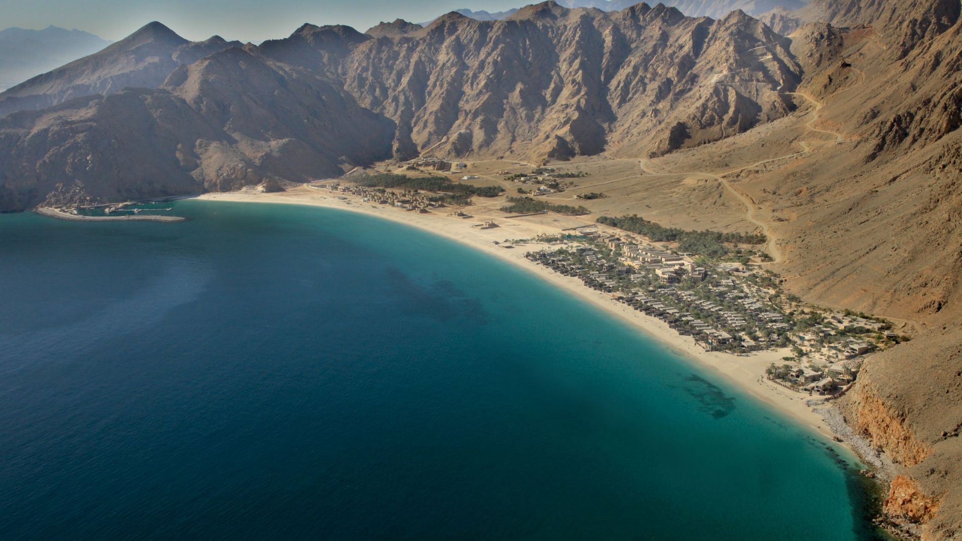 Luftaufnahme von Zighy Bay: türkisfarbene Bucht, Sandstrand, Resorts am Ufer und umliegende Bergketten.
