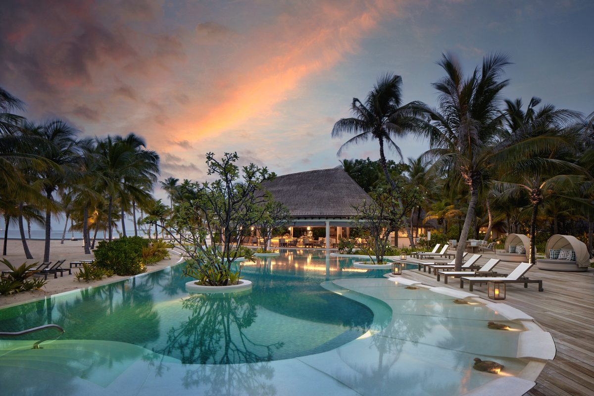 Abend am Pool eines Six Senses Resorts: Palmen, Pavillon mit Strohdach, Liegen, Cabana-Sitze, Inseln im Wasser.