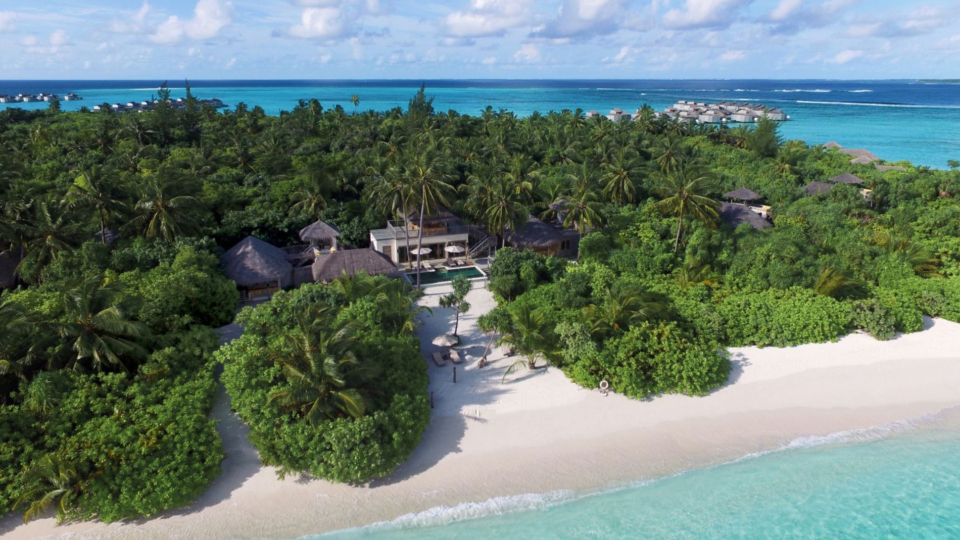 Luftaufnahme von Six Senses Laamu: tropische Insel mit Palmen, Strand, Bungalows; türkisblaues Meer im Hintergrund.