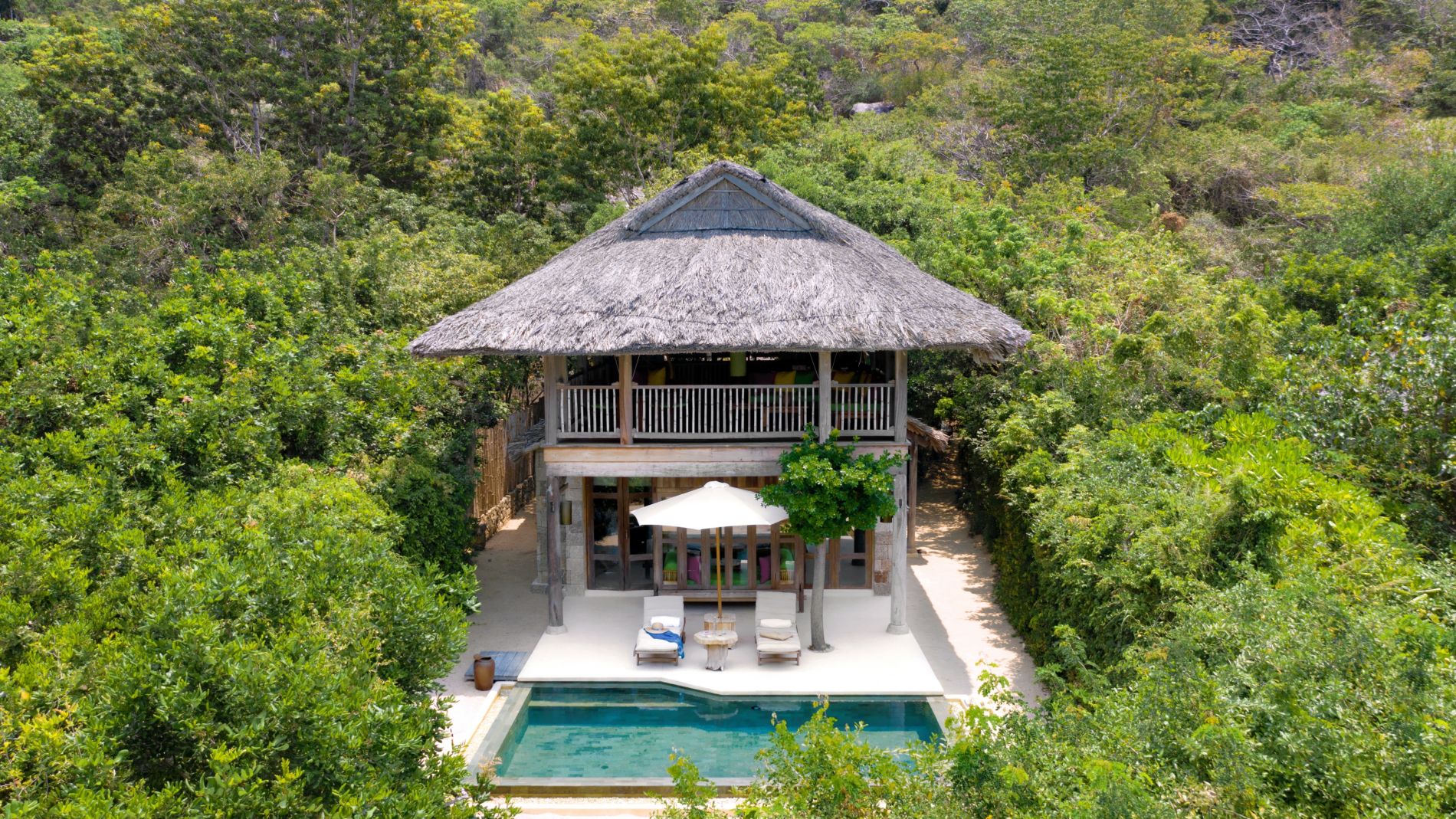 Six Senses Ninvan Bay: Zweistöckiges Strohdach-Haus mit Pool, Liegen und Sonnenschirm, von dichtem Dschungel umgeben.