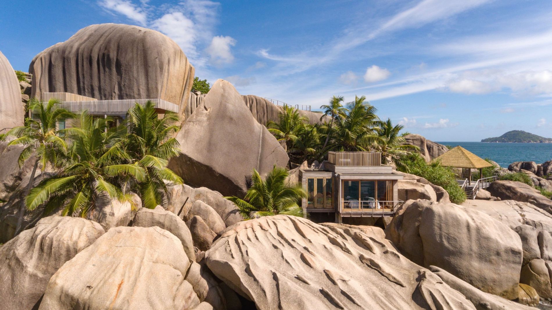 Spa-Exterieur: Villa zwischen riesigen Granitfelsen, Palmen, Glasgebäude am Meer und Reetdach-Pavillon