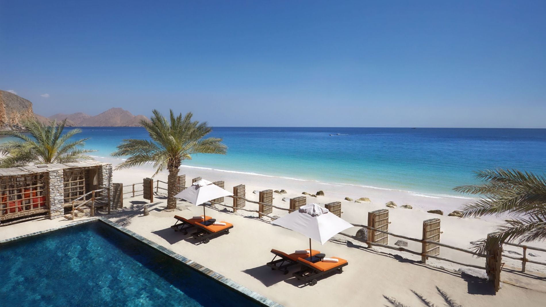 Außenansicht eines Three-Bedroom Beachfront Retreat am Zighy Bay: Pool, Palmen, Sonnenschirme, Strand und Meer.