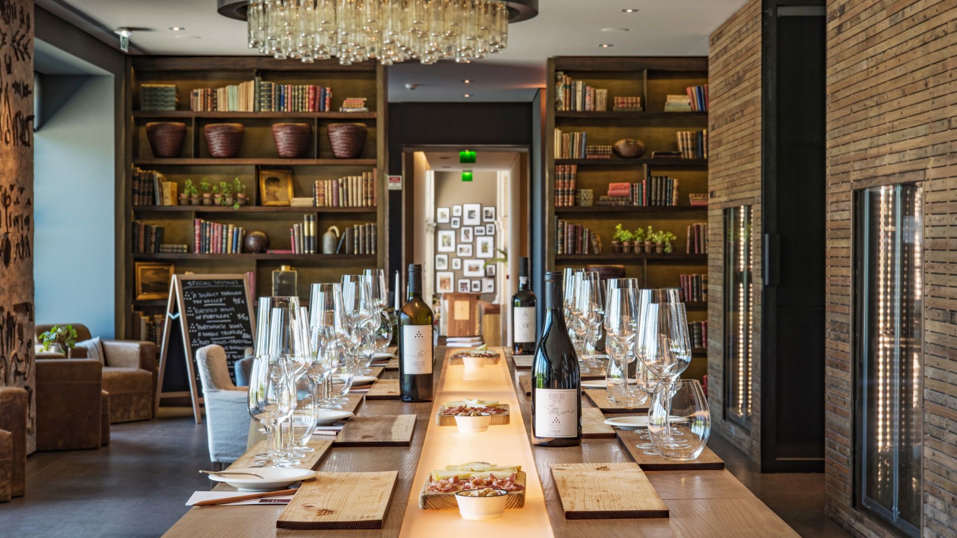 Lange Holztischtafel mit Weinflaschen, Gläsern und Snacks in einem Douro Valley Bibliotheksraum; Six Senses.