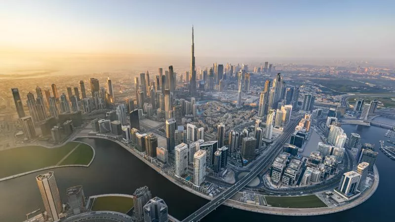 Luftaufnahme Dubais Skyline mit Burj Khalifa im Zentrum, Wasserkanäle, Brücken und Hochhäuser bei Sonnenaufgang.